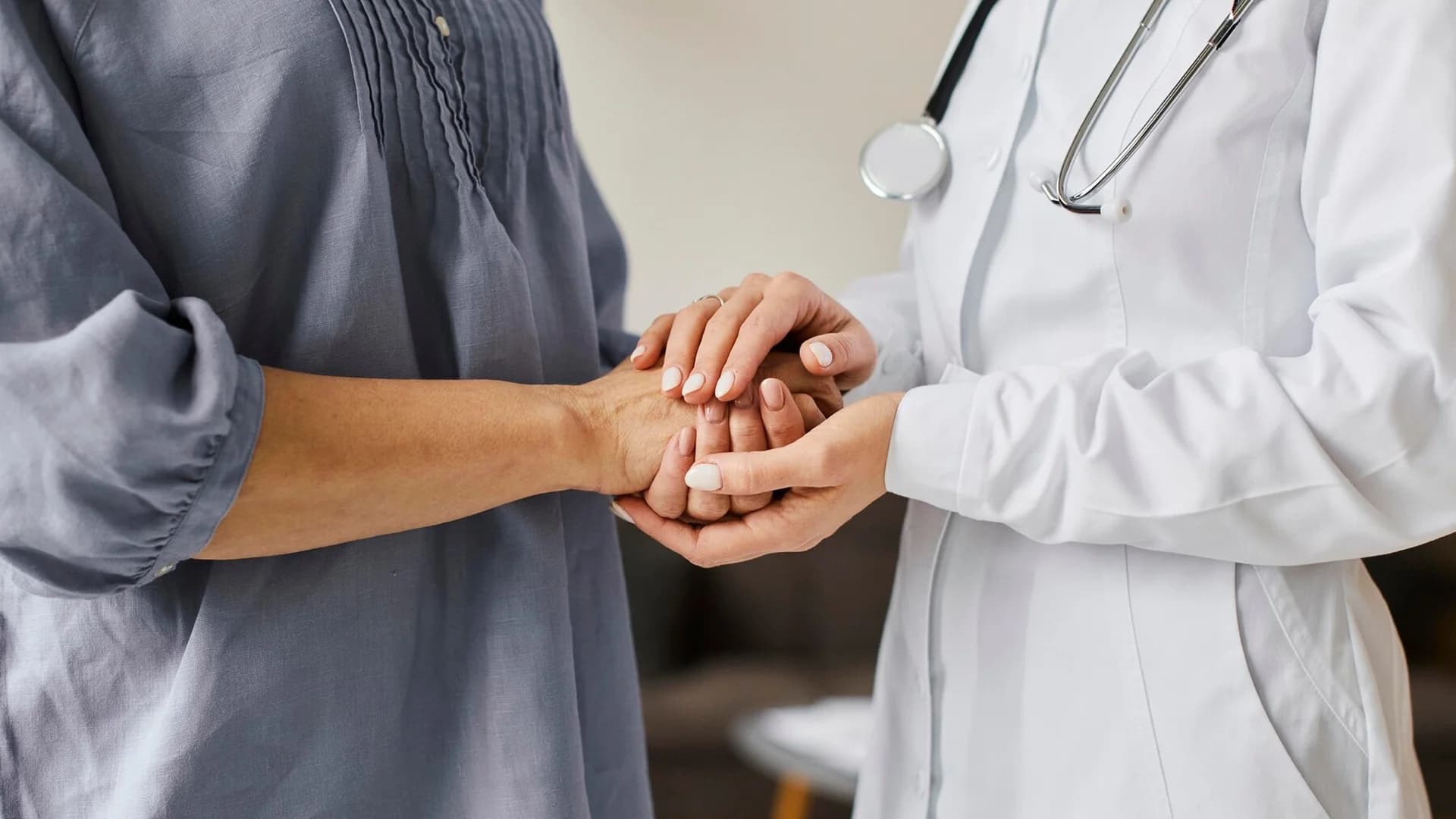 Provider and patient holding hands, representing compassionate, person-centered care.