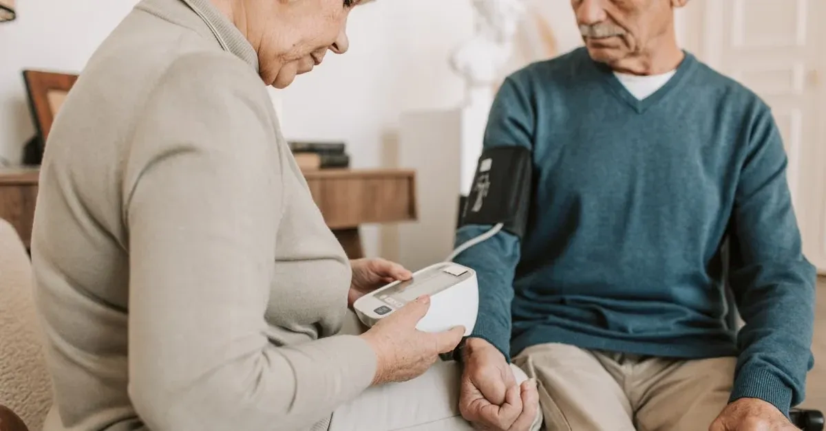 Senior woman checking blood pressure monitor while man watches, reducing hospital readmissions through remote monitoring.