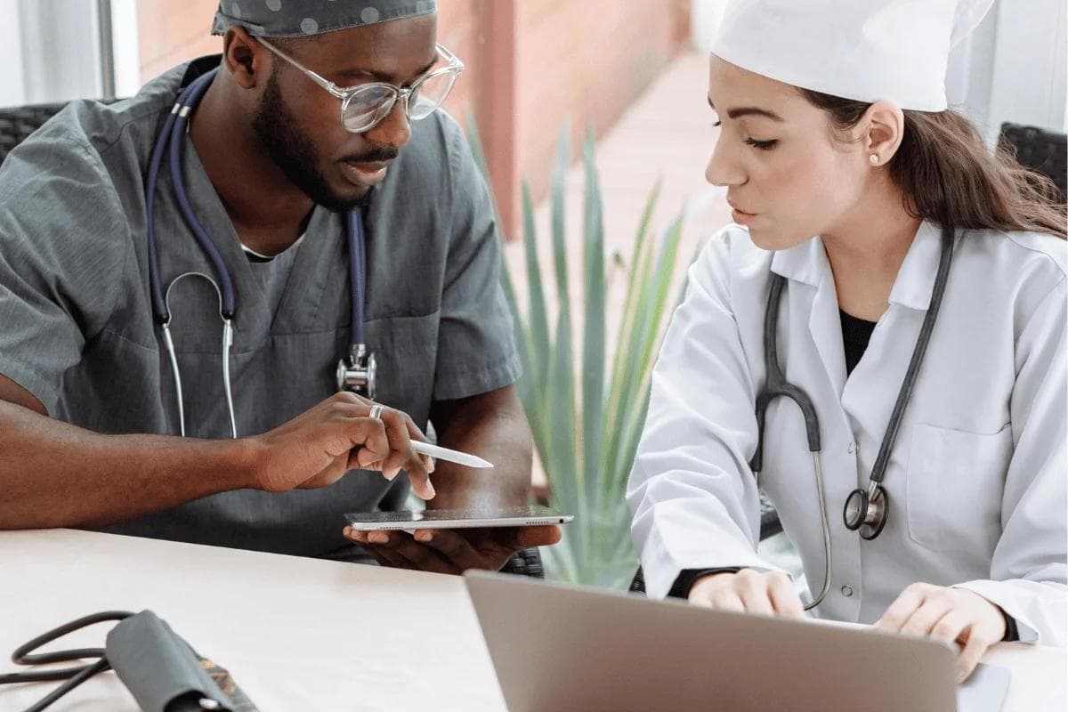 Two healthcare professionals discussing patient data on tablet and laptop.