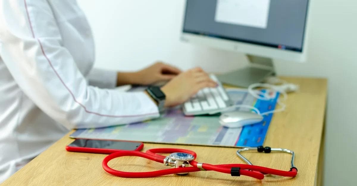 Doctor using keyboard at desk with stethoscope and medical charts, representing ACO reach program management.