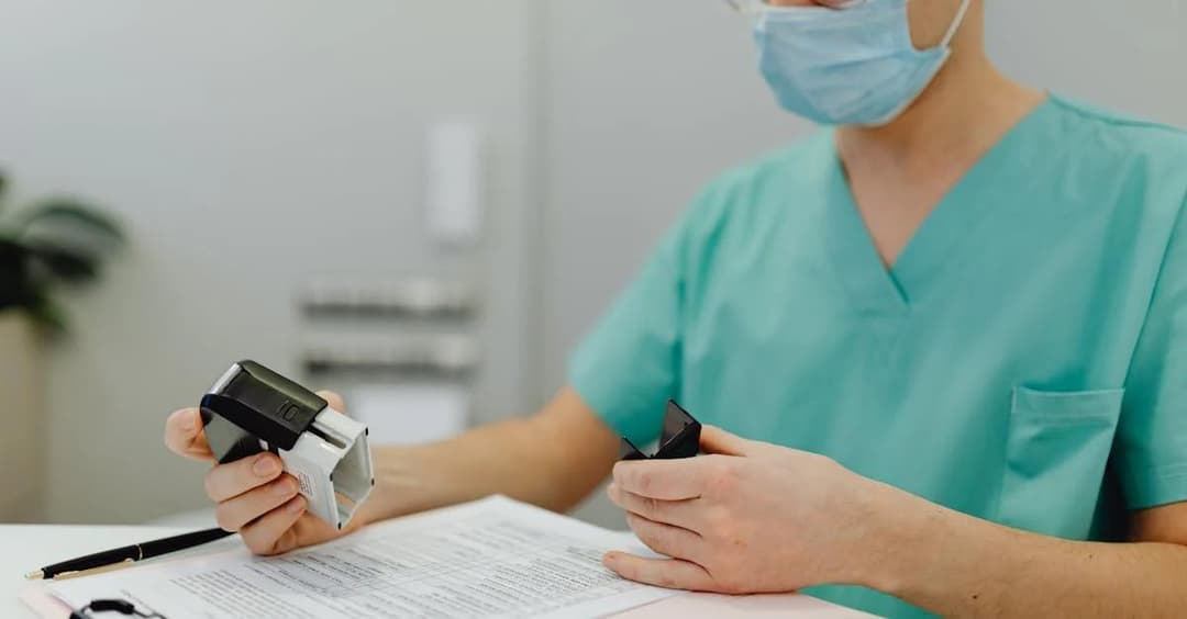 Healthcare professional using remote patient monitoring device at desk with medical clipboard and documentation.