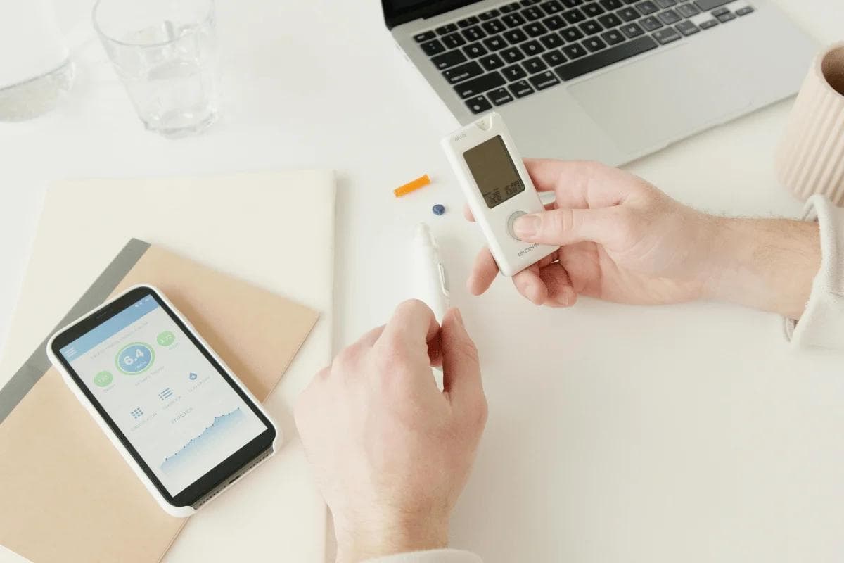 Person using glucose meter next to smartphone app.