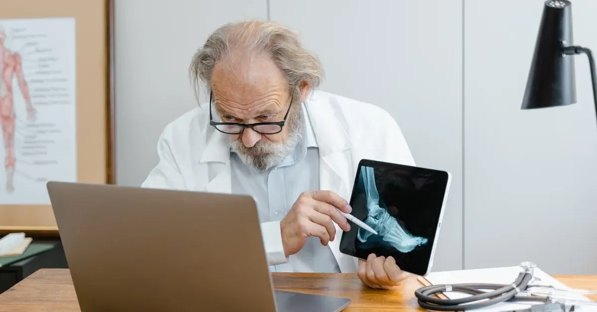 Doctor reviewing digital foot scan on tablet while working with laptop at desk.