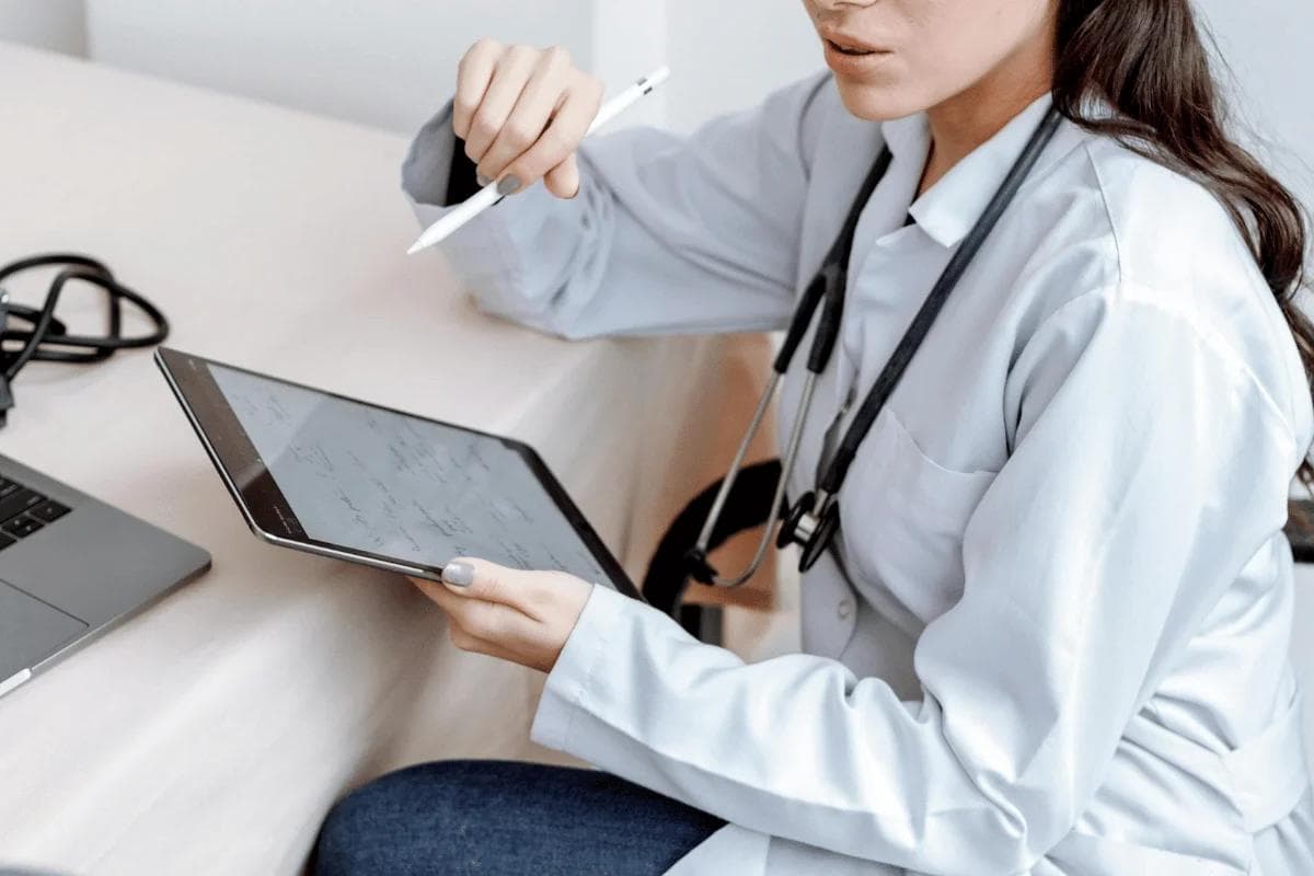 Medical professional in white coat reviewing tablet records.
