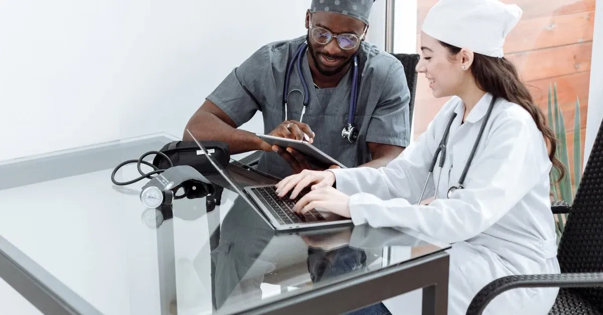 Two healthcare professionals review patient data on laptop at clinic desk, implementing value based care strategy.