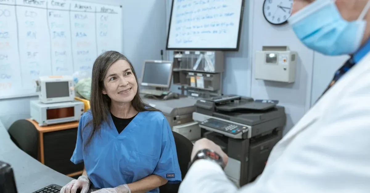 Medical coder in scrubs reviewing CCM documentation requirements at computer in clinical office.