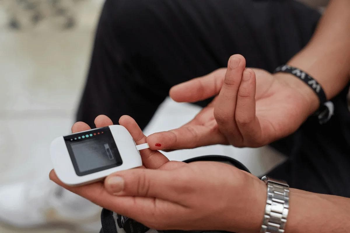 Person testing blood sugar with glucose meter and drop of blood on finger.