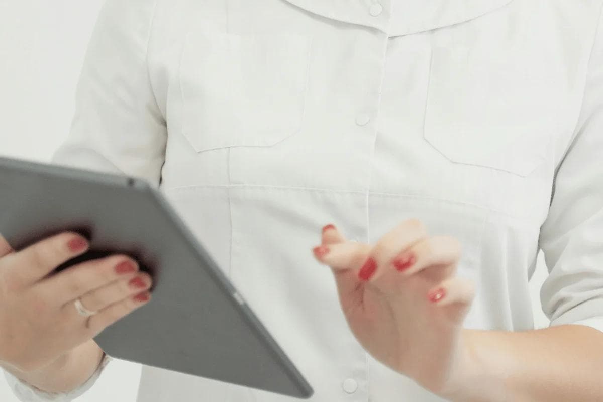 Person in a white lab coat uses a tablet, holding it with one hand and tapping with the other.