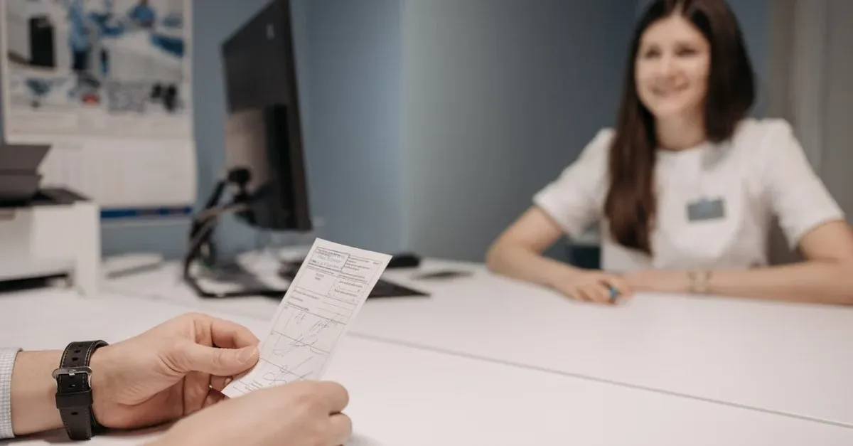 Patient holding insurance card at healthcare reception desk with payment models paperwork and staff member.