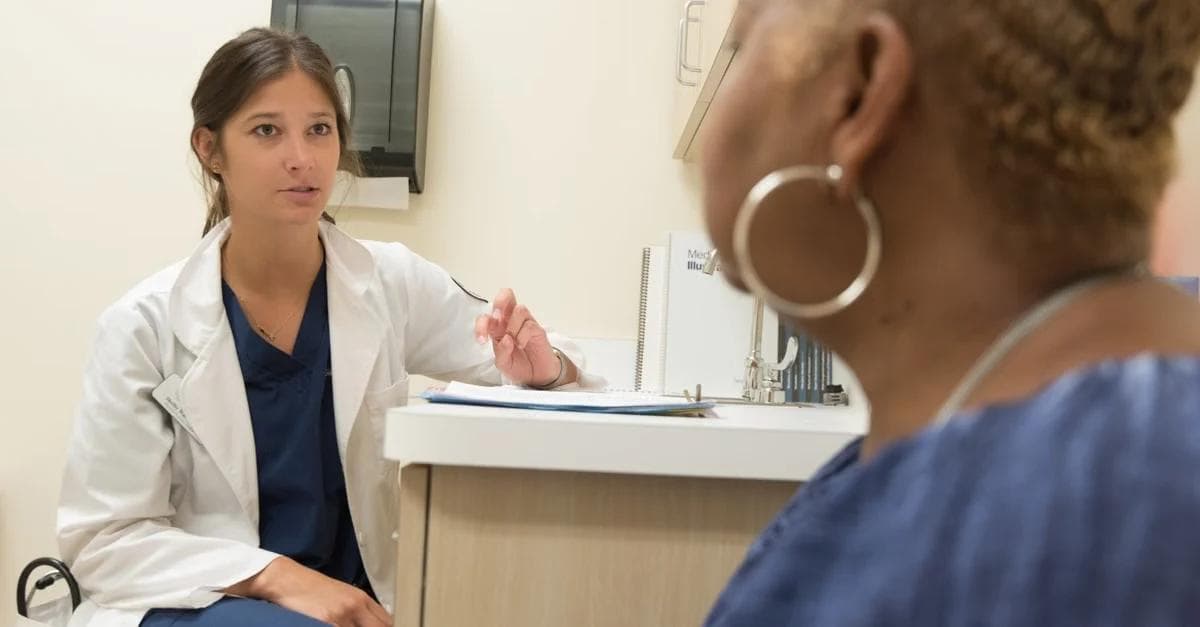 Female healthcare provider in white coat discussing FQHC remote patient monitoring with patient in clinical exam room.