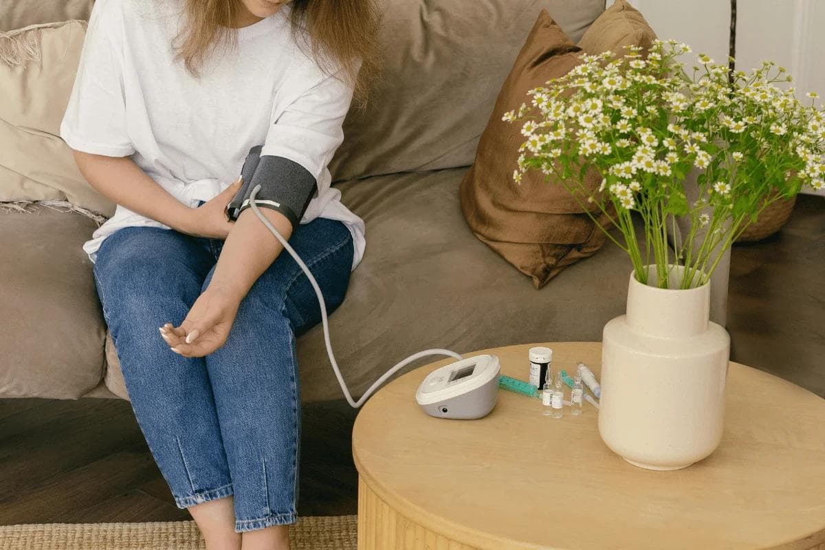 Woman sitting on couch using digital blood pressure monitor at home.