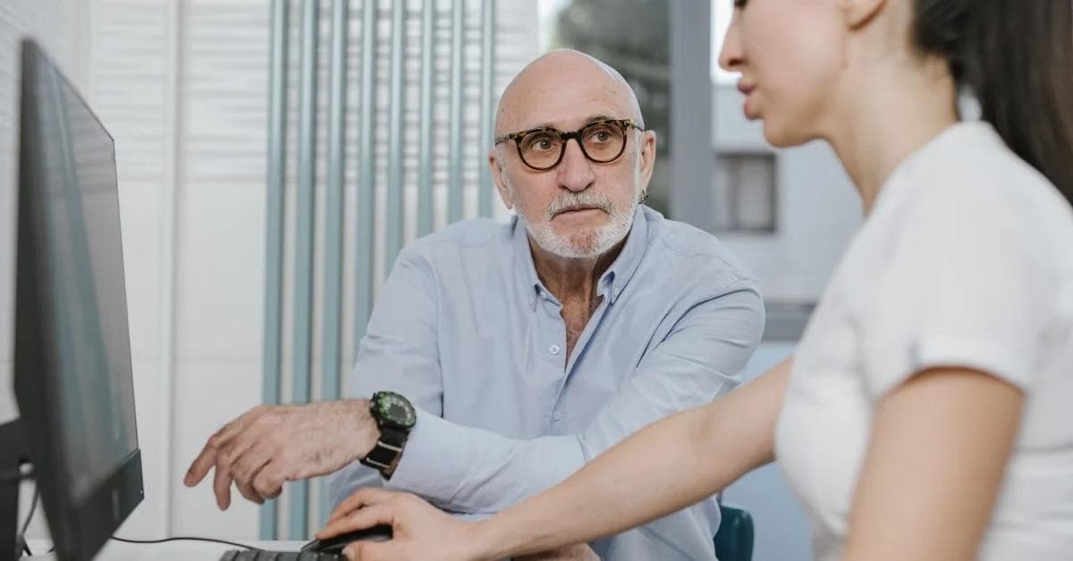 Senior man and woman reviewing medicare guide program information together at desktop computer in office..