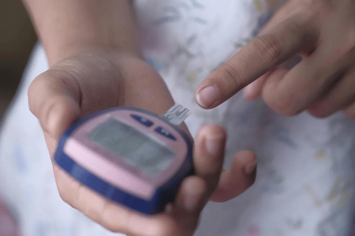 Person holding glucose meter with test strip ready.