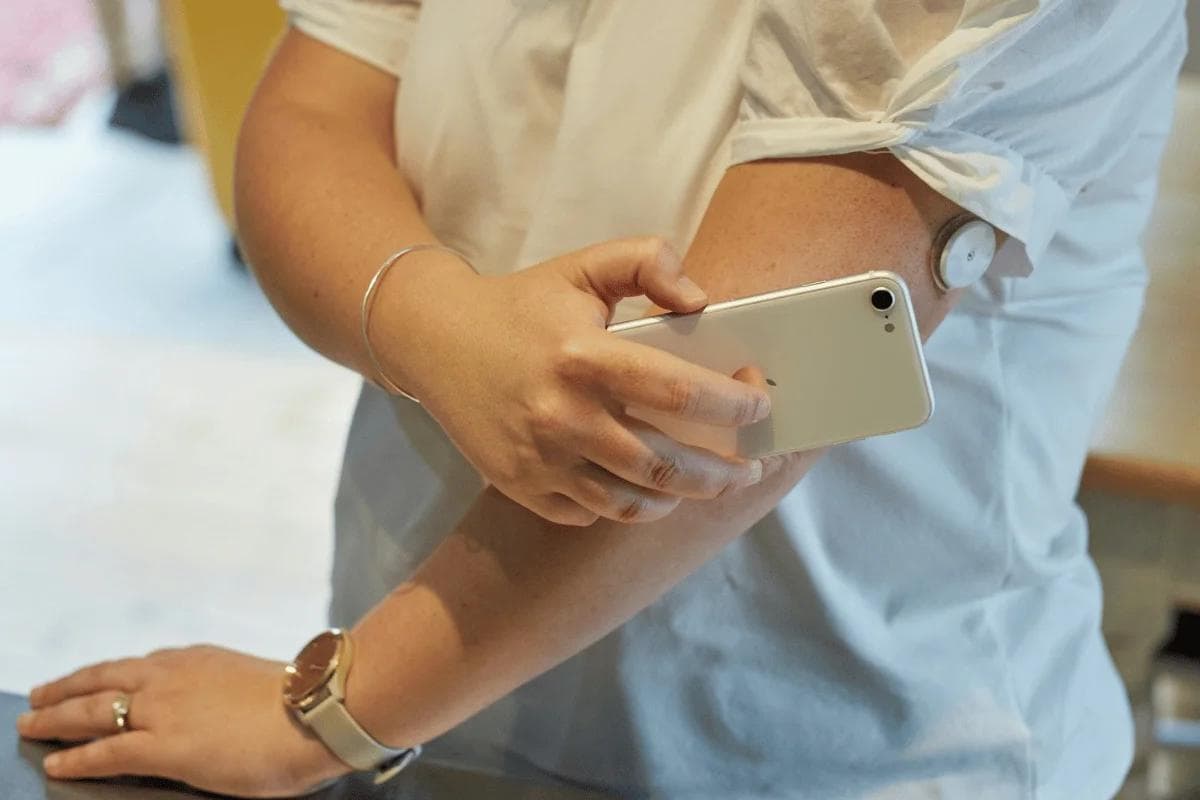 Person scanning glucose monitor sensor on arm using smartphone.