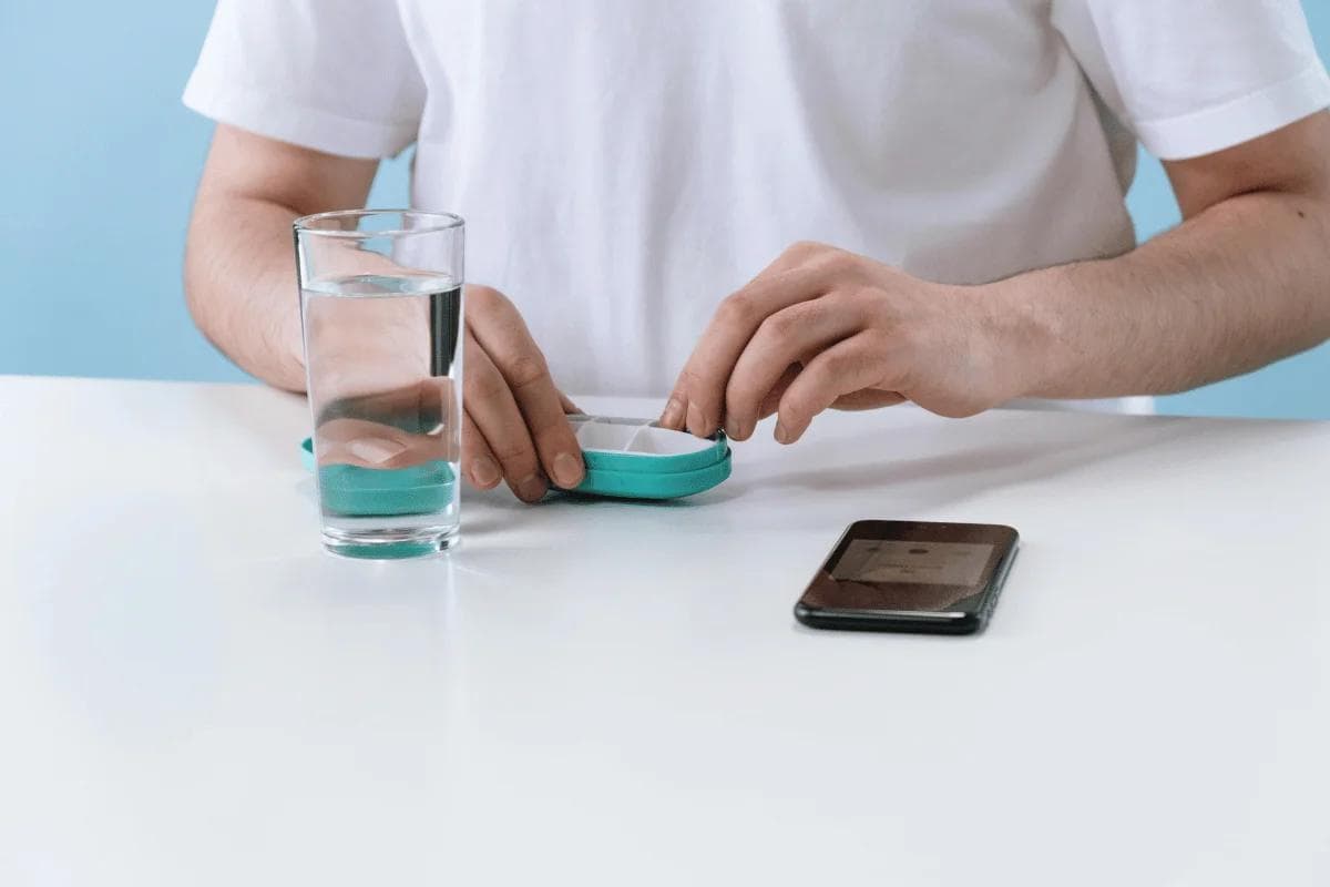 Person organizing pills in a medication case with water and phone.